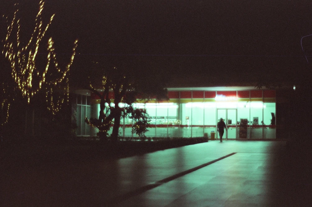 Illuminated Glass Building Through Night Trees. Shot with Olympus OM-1, Olympus Zuiko 50mm f/1.8, Cartenz 200 film